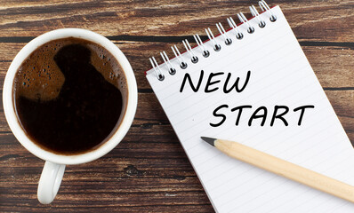 NEW START text on notebook with coffee on the wooden background