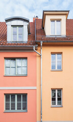 Two rows of 3 windows from two colorful buildings and a drain pipe in the middle of the facade