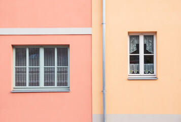 Two windows from two colorful buildings and a drain pipe in the middle of the facade