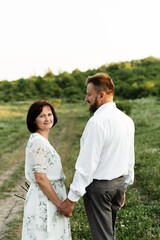 Obraz premium adult couple in love hold hands and walk in nature at sunset of the day. parents are happy. elderly couple.middle-aged couple