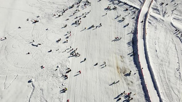A lot of people having fun on mountain. Group of tourists walking, skiing and sledding slope in winter. Aerial drone view of children on the snow. Winter holidays.