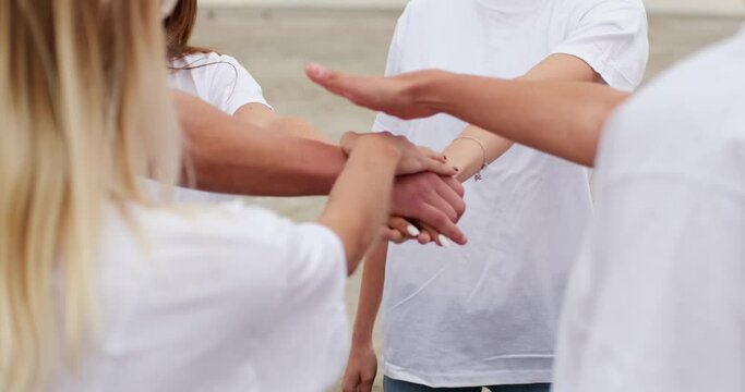 Young men in white T-shirts join their hands together in the center of a circle in front of them. Uniting people into a team.