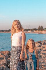 Fototapeta na wymiar Mom with her blonde daughter on the seashore at sunset. Summer rest and entertainment