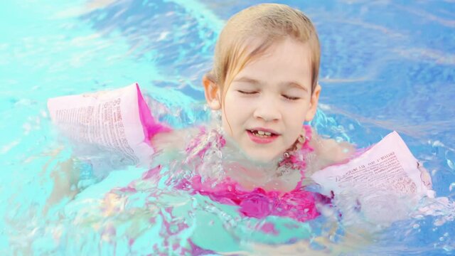 a funny little girl swims and plays in inflatable armbands in a pool