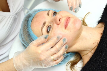 Obraz na płótnie Canvas Beauty salon. A cosmetologist in medical gloves and protective mask doing a hydra peeling procedure on the client's cheeks. Side view. Close up. Professional skin care during coronavirus pandemic.