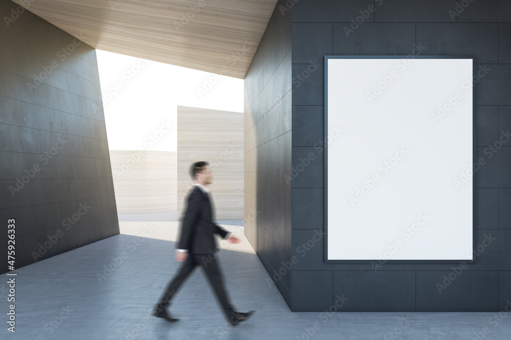 Poster Businessman walking in abstract concrete tile space interior background with empty white mock up poster and sunlght. Design and abstraction concept.