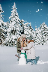 Mother and daughter build a snowman in beautiful snowy landscape.