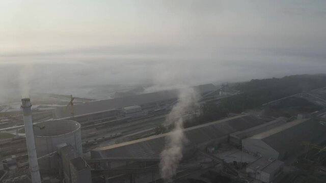 Aerial photo panorama of a drone copter of an industrial factory factory in dense waves of fog at sunrise. Such objects are necessary for the economy, but harmful for ecology.