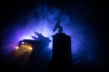Creative artwork decoration. Silhouette of mobile air defence truck with radar antenna during sunset. Satellite dishes or radio antennas against evening sky.