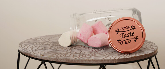 Pink and white marshmallows falling out of a glass jar. 
