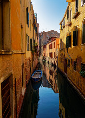 Fototapeta na wymiar Narrow street in Venezia historical town with canal and boat, blue water and old yellow buildings in Italy