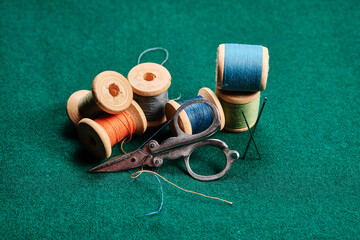 Old wooden spools with multicolored threads and scissors on green cloth. Retro still life....