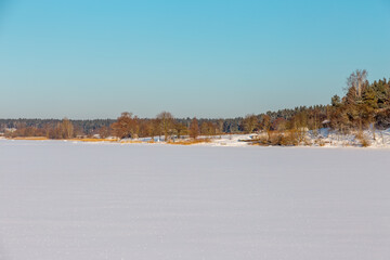 Winter landscape with ice covered lake or river with shores and clear sky