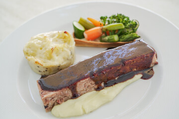 Traditional sirloin with fried mashed potatoes and vegetables with port wine sauce as top view on a modern design plate