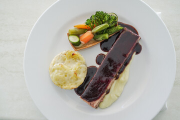 Traditional sirloin with fried mashed potatoes and vegetables with port wine sauce as top view on a modern design plate