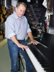 Smiling musician is playing on modern keyboard in music shop.