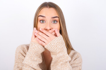 young caucasian girl wearing knitted sweater over white background shocked covering mouth with hands for mistake. Secret concept.