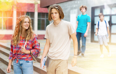 Two positive teens walk along summer street after finishing college lessons