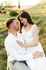 the newlyweds are sitting on a chair and hugging tenderly. girl with a boyfriend on a romantic date at sunset of the day. beautiful couple in the field.