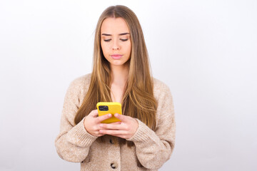 Excited young caucasian girl wearing knitted sweater over white background winking and eye hold smart phone use read social network news