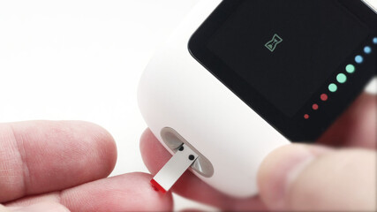 Test of blood sugar level with glucometer for diabetes, finger with blood drop and glucose monitor device, macro shot.