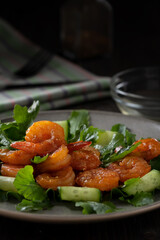 Fresh salad with grilled prawns, cucumbers and arugula, served on a plate, vertical image