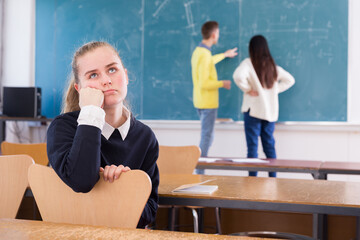 Portrait of tired student girl sitting separately in classroom in break between lessons