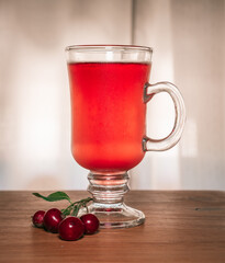 Flavored red fruit cider accompanied by cherries, on a wooden surface