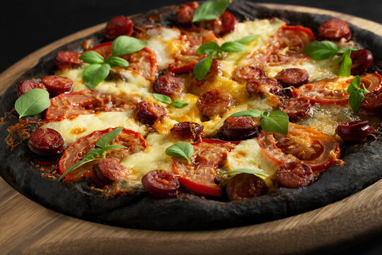 Black pizza with tomatoes, sausages, mozzarella and basil. Dough with healthy bamboo charcoal powder