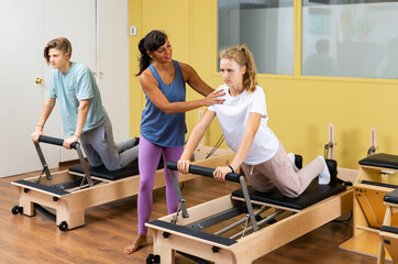 Young boy and girl doing exercises on pilates reformers. Their trainer hispanic woman correcting them.