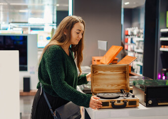Young woman making shopping in musical equipment and instrumental store, examines retro gramophone