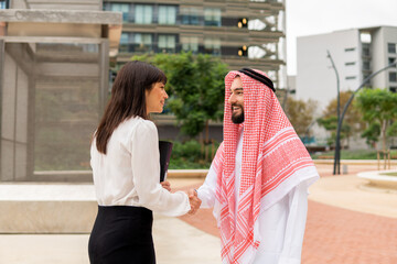 Smiling Arab man shaking hands with european business woman while standing on city street outdoors