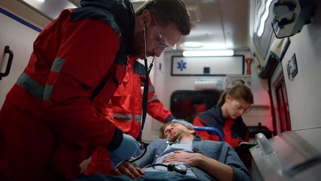 EMS paramedics measuring man blood pressure with tonometer in emergency vehicle