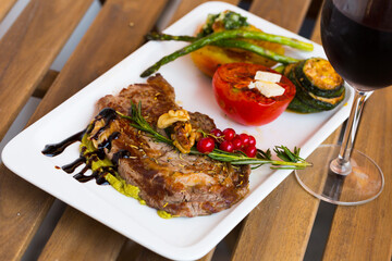 Appetizing grilled veal loin with guacamole and baked vegetables served on ceramic plate on wooden background..