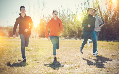 Happy teenage friends having fun together in spring city park, chasing each other on green meadow