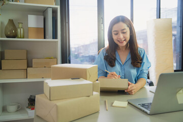 Young business woman working online e-commerce shopping at her shop. Young woman seller prepare parcel box of product for deliver to customer. Online selling, e-commerce.