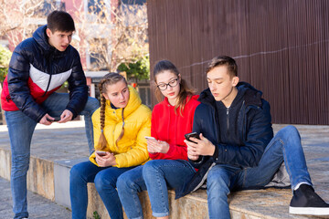 Teenage friends spending time together in city streets in spring, discussing interesting topics and browsing on phones