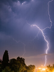 Branched lightning strike against the backdrop of trees and glowing street lamps