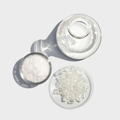 Cetyl esters wax in glass container place next to Sodium Thiosulfate in chemical watch glass and Erlenmeyer flask on laboratory table. Top View