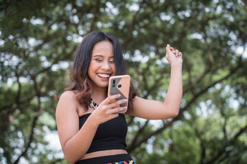 A pretty Filipina woman celebrates upon seeing great news on her phone. Receiving a notification...
