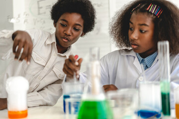 Two african american cute little boy and girl student child learn science research and doing a chemical science experiment making analyzing and mix liquid in test tube on class at school