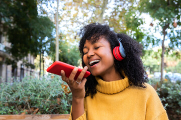 Laughing young African American woman sending a voice message using mobile phone.