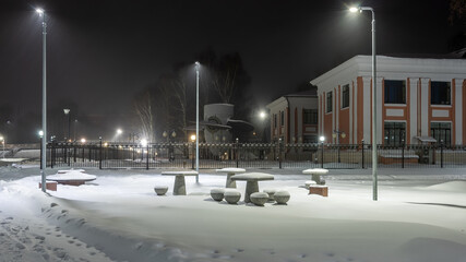 Stone tables and chairs for playing chess and relaxing covered with snow in a winter park.