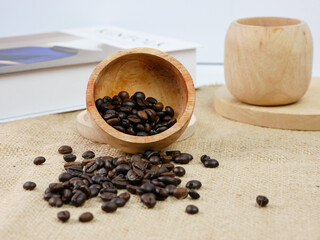 Wooden cup of coffee with coffee beans and book with blur background.