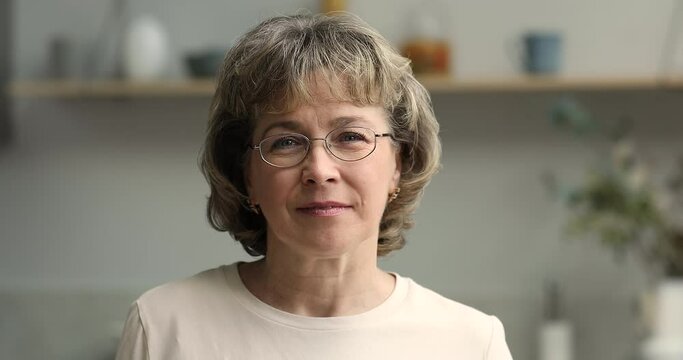 Beautiful middle aged female retiree in eyewear look at camera with sincere candid smile show white even teeth satisfied with good result of beauty skin face care procedures. Headshot video portrait