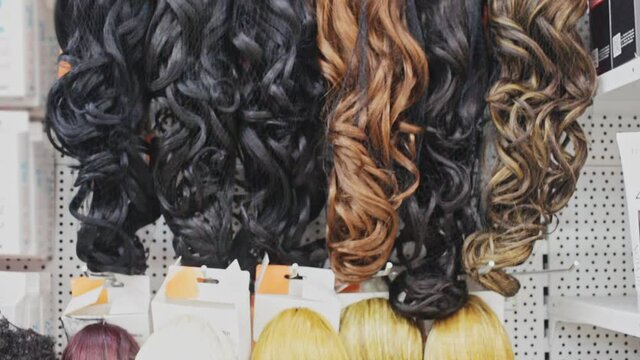 Variety of natural wigs and hairpieces hanging on stand in specialized store. High quality FullHD footage
