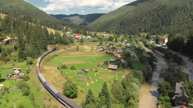 Aerial shot of train passing through village in Carpathian mountains in Ukraine