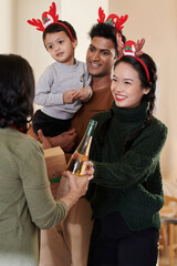 Fototapeta premium Cheerful young woman accepting present and wine her senior mother brought for Christmas