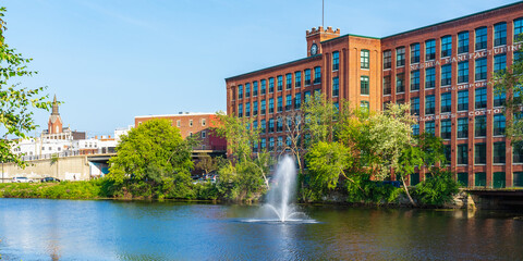 A fountain and a historic cotton factory building with a clock tower in the old industrial park of Nashua. Nashua Corporation. Nashua Manufacturing Company, New Hampshire, USA