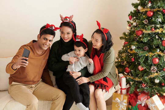 Smiling man in reindeer antlers taking selfie with his family to post on social media